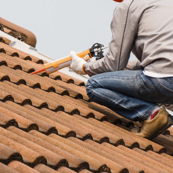 Roofer using a caulk/grout gun during a tile roof installation.